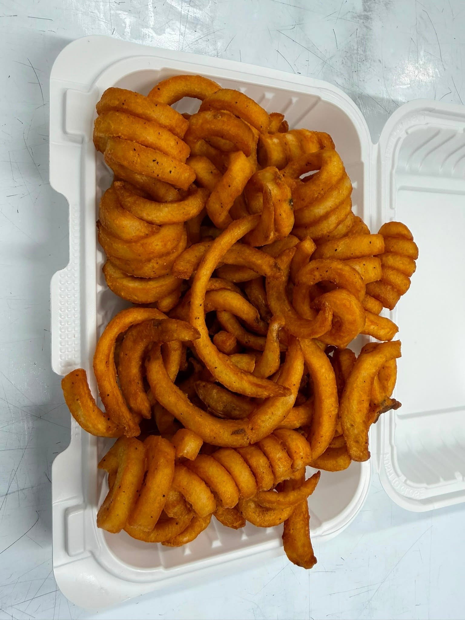 A takeout box filled with golden Salty’s curly fries